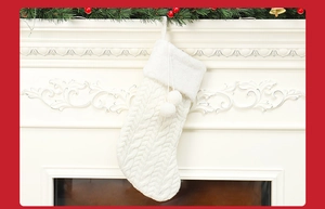 Detail of off-white knitted Christmas stocking with pom-poms on a white fireplace