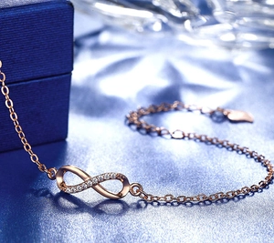 Macro shot of rose gold infinity charm bracelet with sparkling zircons on blue base