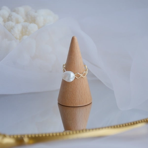 Detail of 14k gold-plated wave ring with natural freshwater pearl on wood stand