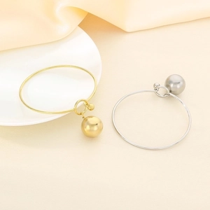 Detailed close-up of minimalist gold and silver bangles with ball pendants on silk fabric