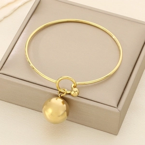 Close-up of golden metallic bangle featuring a large hollow sphere pendant and round knot