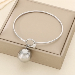 Close-up of polished silver bangle with hollow ball pendant on a beige jewelry box