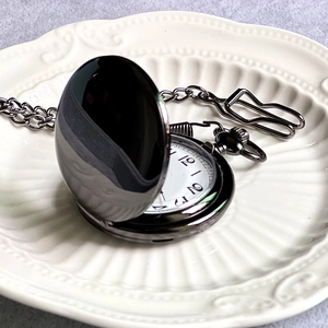 Vintage Alice in Wonderland style black metal pocket watch on white embossed ceramic plate