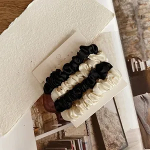 Close-up of four silk satin scrunchies in black and ivory cream on a nyunyu display card