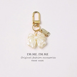 Detail of pearlescent white bow keychain with golden clasp and engraved metal tag