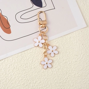 Golden metal keychain featuring white enamel flower charms on a beige textured surface