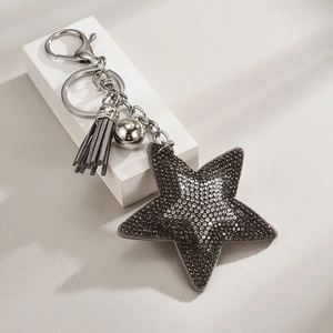 Detail shot of a star keychain with dark grey rhinestones and leather fringe on a white block