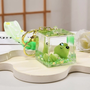 Macro view of clear acrylic keychain cube with green frog figure and liquid glitter