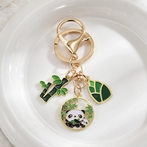 Close-up of panda and bamboo enamel pendants with gold-plated keychain on white plush base