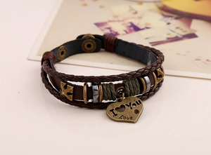 Close-up of woven brown leather bracelet featuring a vintage heart charm with Love engraving