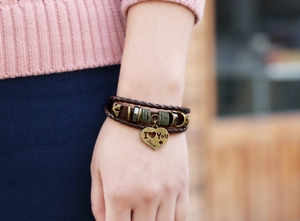 Detail view of multi-layer brown leather bracelet with heart charms on model's wrist