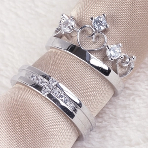 Silver crown and cross couple rings set with clear gems on elegant silk fabric