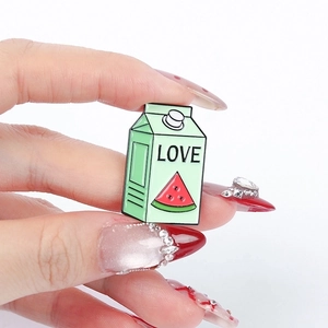 Green milk box enamel pin with watermelon and LOVE pattern held in hand