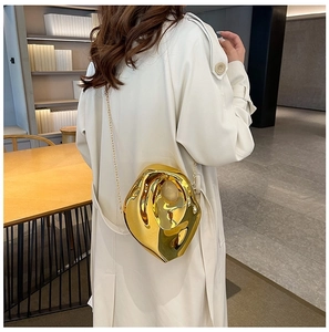 Detail of a modern gold irregular sculpture clutch bag with chain strap on a woman