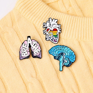 Detail of anatomical heart and brain enamel pins pinned on a yellow knitted sweater