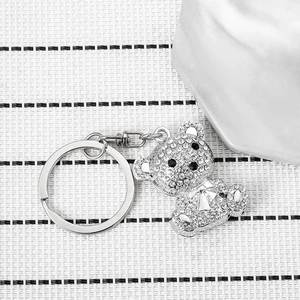 Sparkling crystal bear keychain with silver metal ring and chain on a white textured background