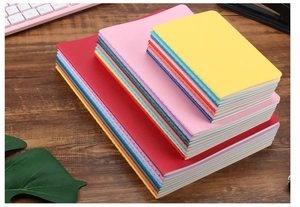 Multi-colored notebooks in A5 and B5 sizes stacked on a dark wood office desk