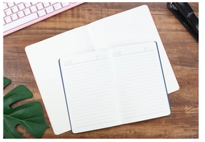 Detail view of A5 and A6 notebooks with lined pages on a wooden desk with office tools