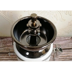 Manual coffee grinder with ceramic body and dark metal bean hopper on wooden surface