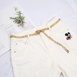 Golden metal chain belt with square buckle accessory on white denim jeans