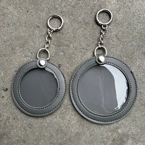 Detail of round grey leather badge holder keychain with clear window on stone surface