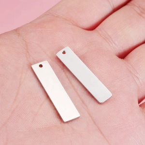 Polished stainless steel rectangular tag pendants held in hand to show scale