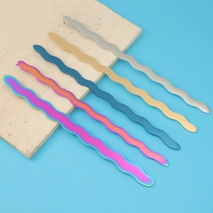 Polished wavy metal massage tools in silver, gold, blue, and rainbow on marble plate