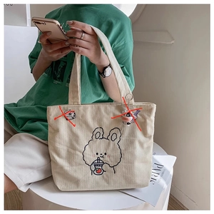 Detail view of beige corduroy tote bag with cartoon rabbit embroidery on a shoulder strap
