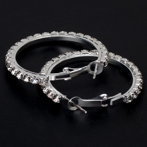 Detail of silver hoop earrings with white rhinestones on a textured black background