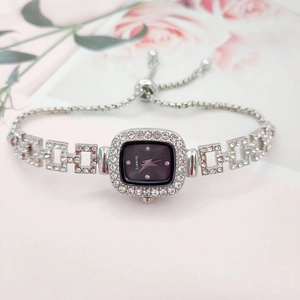 Detail of silver square watch with black dial and crystal straps on floral backdrop