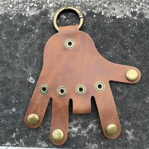 Close-up of brown palm-shaped leather keychain with brass snaps on concrete surface