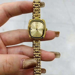 Detail of gold rectangular watch dial with woven chain strap and Roman numeral XII
