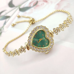 Macro detail of a heart-shaped gold watch with green dial and sparkling rhinestones