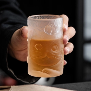 Frosted glass tea cup with cute embossed cat and persimmon motifs in hand-held macro view