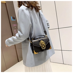 Detail of a black leather crossbody bag with a golden lion head clasp on a fashion model