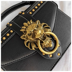Macro detail of black lychee leather crossbody bag with golden lion head and rivets
