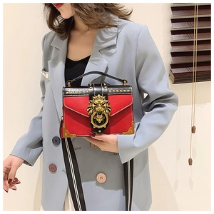Close-up of red and black leather bag featuring a gold lion head and striped strap
