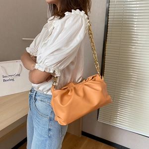Detail of orange cloud pouch bag with thick gold chain strap worn under the arm