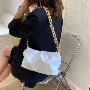 White pleated cloud bag with chunky gold chain strap worn over a black blazer