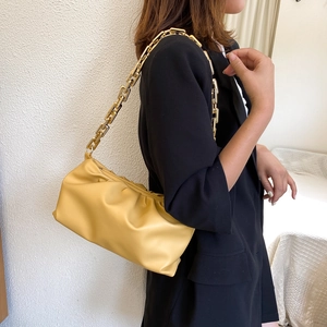 Detail of yellow pleated cloud bag with chunky gold chain strap shown on model shoulder
