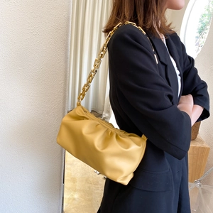 Detail of a yellow pleated cloud bag with a chunky gold chain strap worn on the shoulder