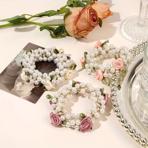 Three elegant pearl hair scrunchies with fabric roses and ribbons on a soft background