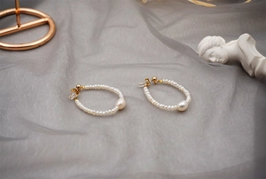 Macro detail of freshwater pearl hoop earrings on elegant grey silk background