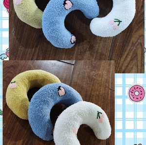 Close-up of soft U-shaped pet pillows in yellow, blue, and white with embroidered patterns