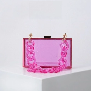 Detail of bright pink acrylic box clutch with chunky chain strap on white platform