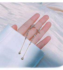 Detail of geometric silver needle tassel earrings with zircons on white fabric