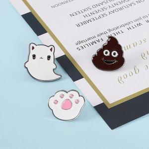 Cute enamel pin set featuring white ghost cat, brown emoji and pink paw prints