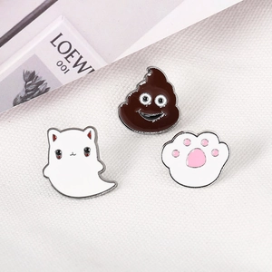 Cute enamel pins set with cat paw, ghost, and poop designs on white textured fabric