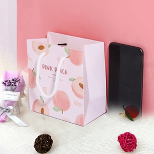 Detailansicht der rosa Pfirsich-Geschenktüte mit weißen Kordelgriffen und dekorativen Elementen
