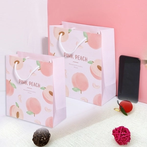 Detailansicht von rosa Pfirsich-Geschenktüten in zwei Größen mit weißen Griffen und Muster